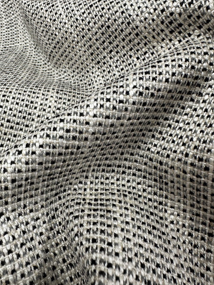 Close-up of Upholstery Logan - Salt & Pepper - 145cm from Super Cheap Fabrics, featuring a black and white checkered open-weave grid. This heavyweight woven material displays textured folds, creating an undulating surface.