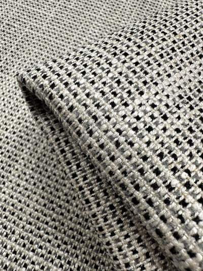 A close-up of Super Cheap Fabrics' Upholstery Logan - Salt & Pepper - 145cm shows its black and white checkered weave, ideal for heavyweight upholstery. The slightly folded fabric highlights its structure, making it a perfect textured accent piece.