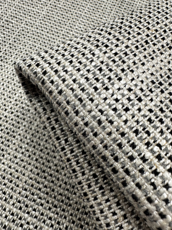 A close-up of Super Cheap Fabrics' Upholstery Logan - Salt & Pepper - 145cm shows its black and white checkered weave, ideal for heavyweight upholstery. The slightly folded fabric highlights its structure, making it a perfect textured accent piece.