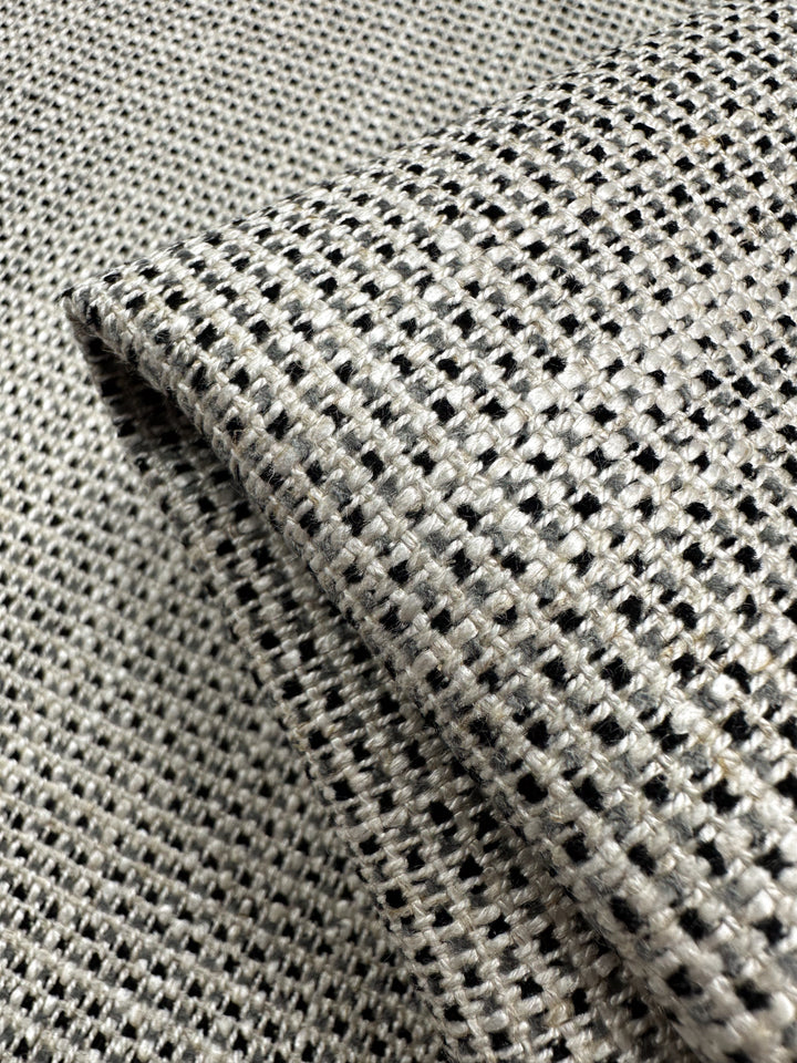 A close-up of Super Cheap Fabrics' Upholstery Logan - Salt & Pepper - 145cm shows its black and white checkered weave, ideal for heavyweight upholstery. The slightly folded fabric highlights its structure, making it a perfect textured accent piece.