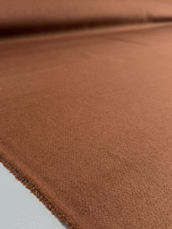 A close-up of Super Cheap Fabrics' Wool Cashmere - Dark Hazel - 150cm shows its soft, slightly fuzzy brown texture and luxurious edge laid flat, highlighting the premium quality fabric.