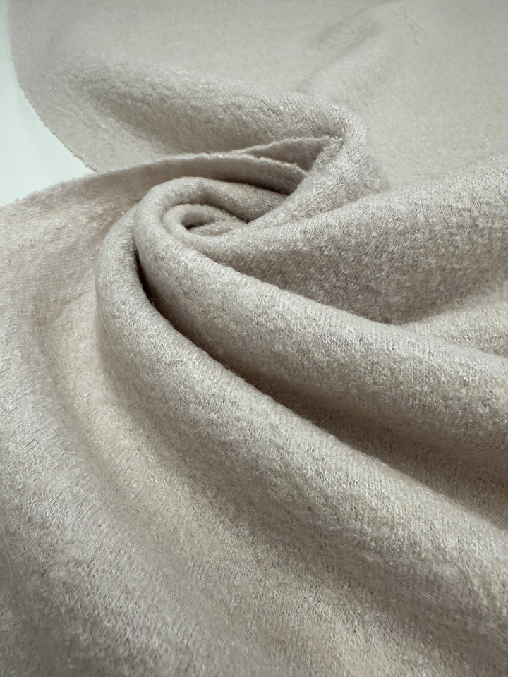 Close-up of the Boiled Wool - Coconut Milk - 140cm by Super Cheap Fabrics, showcasing its soft, light beige texture with fuzzy elegance, draped and twisted to form gentle folds and curves for a cozy warmth.