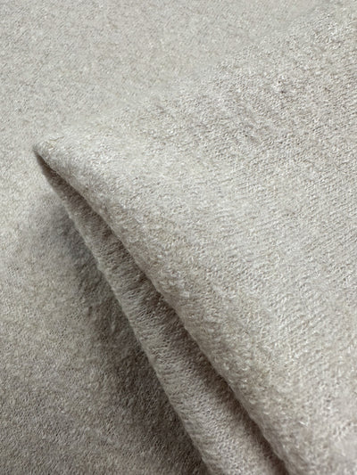 Close-up of Super Cheap Fabrics' Boiled Wool in Coconut Milk, 140cm wide. The heavy weight wool fabric appears soft and light gray with a warm, fluffy texture and visible folds that highlight its plush and cozy quality.