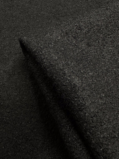 Close-up of Super Cheap Fabrics' Boiled Wool - Black - 145cm, showing its dark, textured appearance. The folded material highlights its thick and dense weave, with lighting emphasizing its rich color.