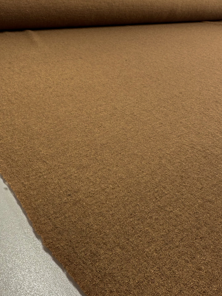 A close-up of Super Cheap Fabrics' Boiled Wool in Tobacco displays its textured brown surface, laid out flat and extending seamlessly into the background.