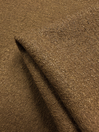 Close-up of Super Cheap Fabrics' Boiled Wool - Tobacco - 145cm, showcasing its rough, woven texture. The folded fabric highlights thickness and grainy surface, and lighting emphasizes details, suggesting it's suitable for warm garments.