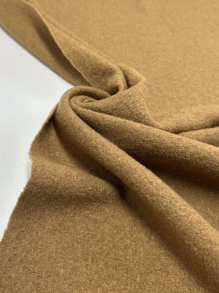 A close-up of Super Cheap Fabrics' Boiled Wool in Oak, a soft light brown 147cm wool-viscose blend with a slightly rough texture, draped on a white surface to highlight its flexibility and thickness.