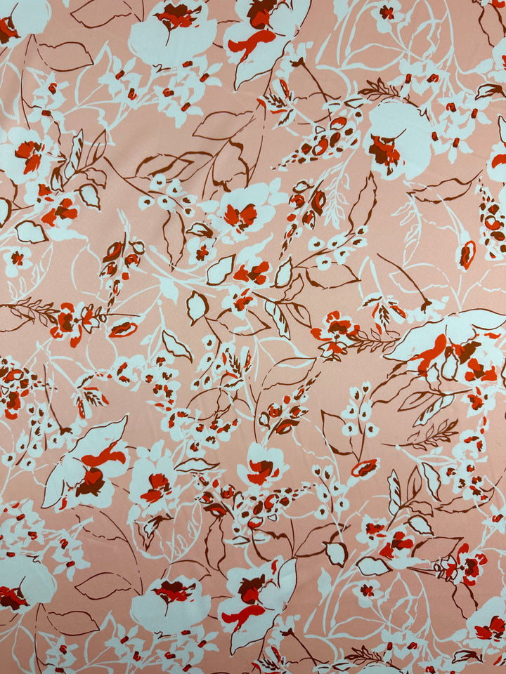 The Printed Stretch Satin - Pink Sakura from Super Cheap Fabrics features elegant pieces with red, white, and brown florals and leaves on peach, showcasing various sizes of blossoms and foliage in an intricate, lively design. Width: 150cm.
