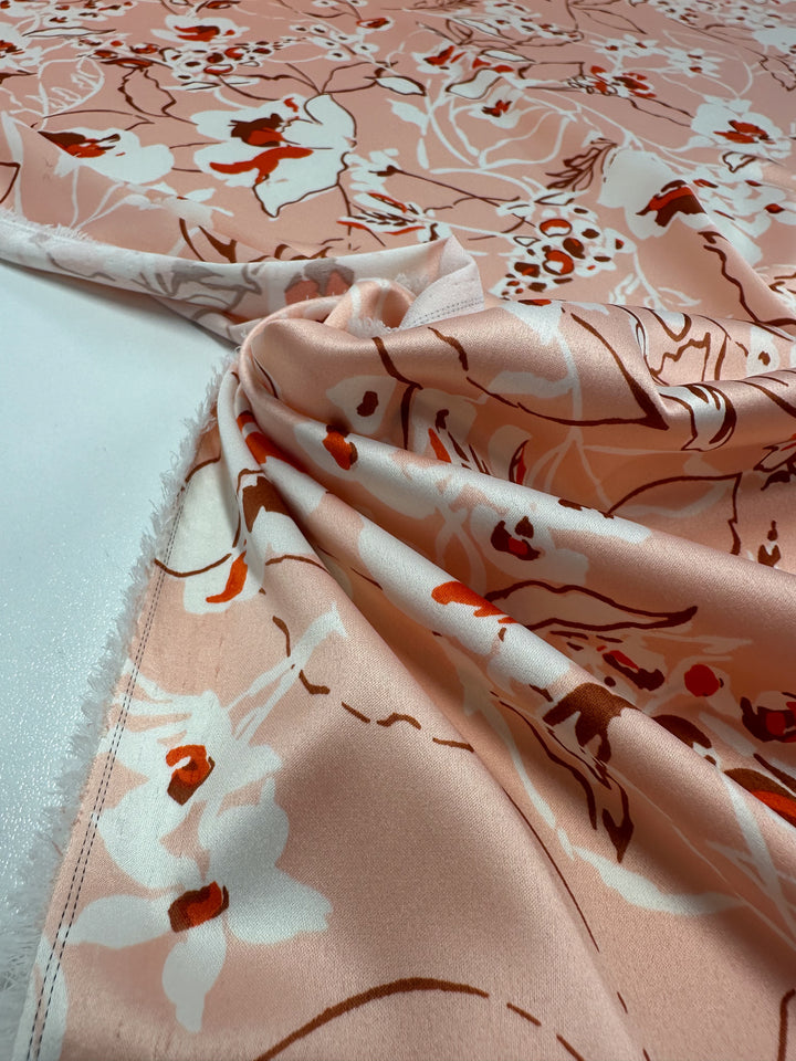 A close-up of Super Cheap Fabrics' Printed Stretch Satin - Pink Sakura, showcasing its pink floral pattern with white and red flowers on brown stems. This 150cm lightweight fabric is beautifully gathered on a white background.