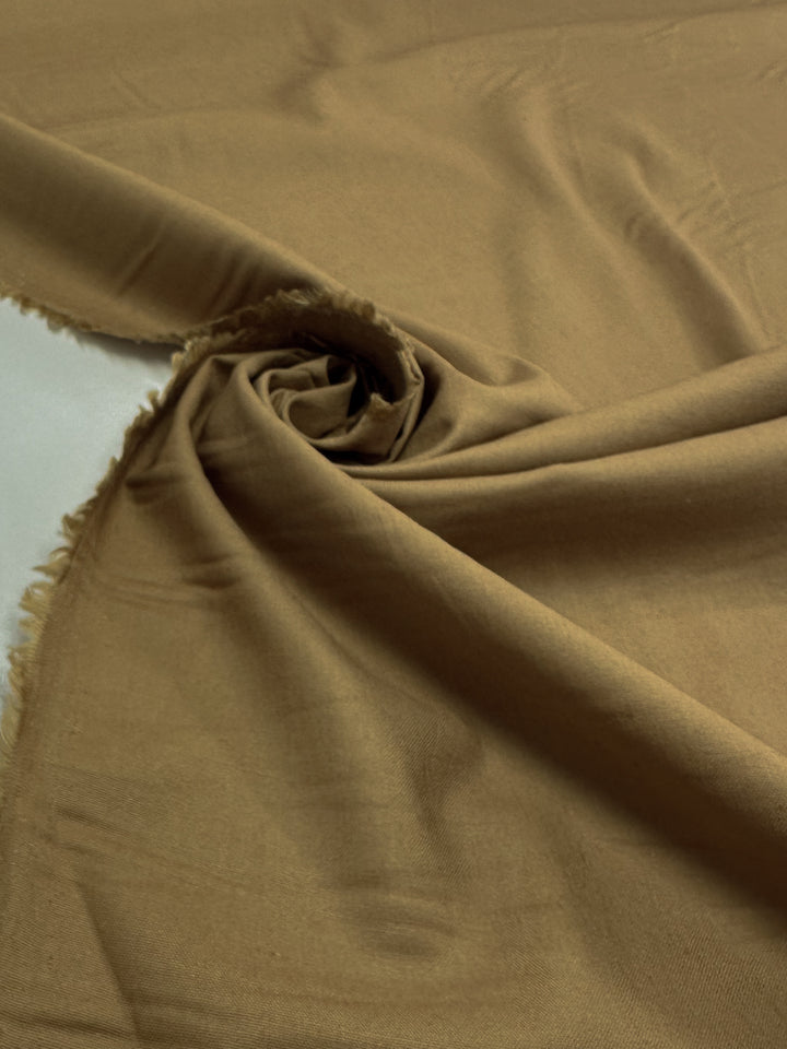 The Linen Blend - Dijon - 137cm from Super Cheap Fabrics features a medium weight with a spiral twist at the center. Edges are slightly frayed, adding texture to its smooth surface.