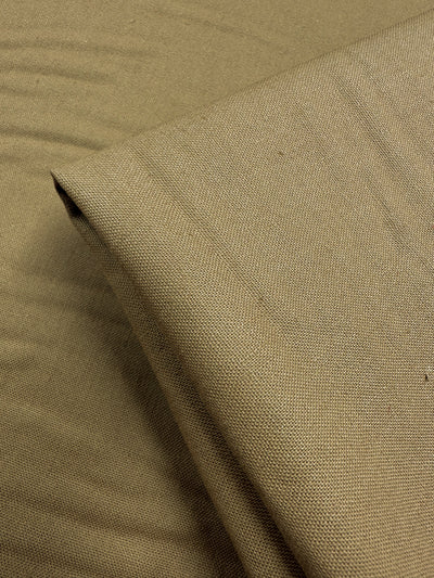 A close-up of the folded Linen Blend - Dijon by Super Cheap Fabrics shows its smooth texture and visible weave, crafted from a linen-cotton mix. With a slightly wrinkled backdrop of the same fabric, it offers a monochromatic look ideal for medium-weight drapery or upholstery.