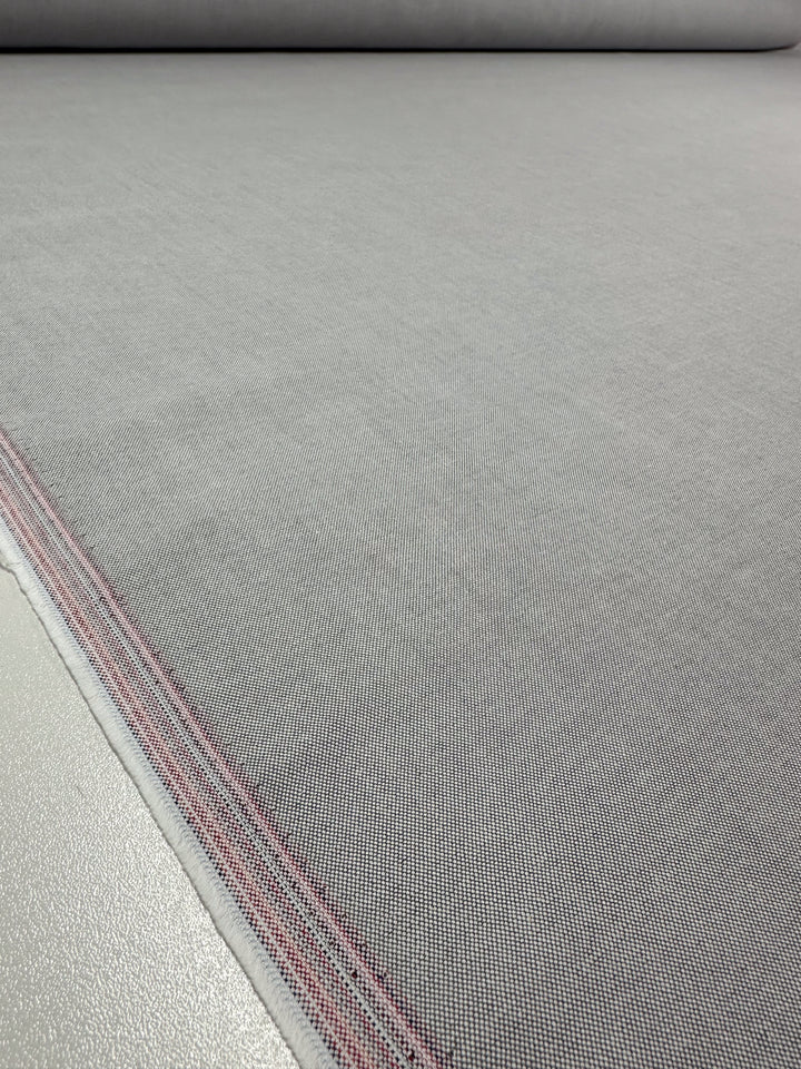 A close-up of the Linen Blend - Grey White - 150cm fabric from Super Cheap Fabrics displays its subtle grid pattern with a red edge stripe as it lies elegantly on a smooth surface.