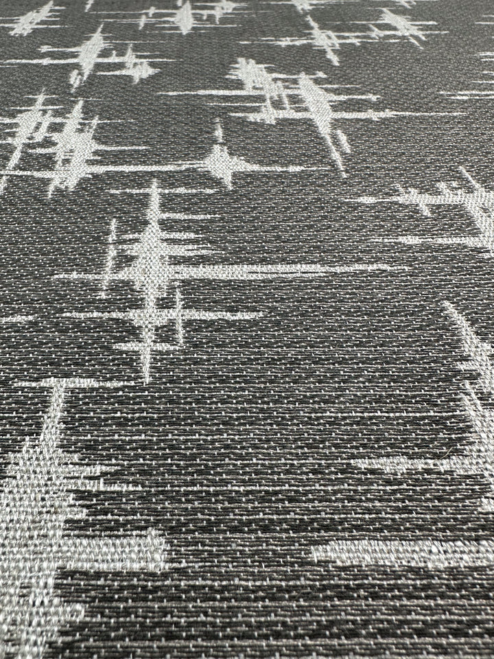 A close-up of Super Cheap Fabrics' Abstract Woven Upholstery - Morissey - 147cm reveals a textured fabric with abstract, intersecting light gray lines on dark gray. Its glitch-like pattern complements modern furniture, adding a dynamic touch.