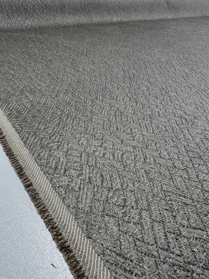 Close-up of Super Cheap Fabrics' Herringbone Textured Upholstery in Urbane Silver. This 143cm wide fabric features a subtle diamond pattern and heavy weight, giving it an elegant drape with a stitched border, reminiscent of sophisticated upholstery as it recedes into the background.
