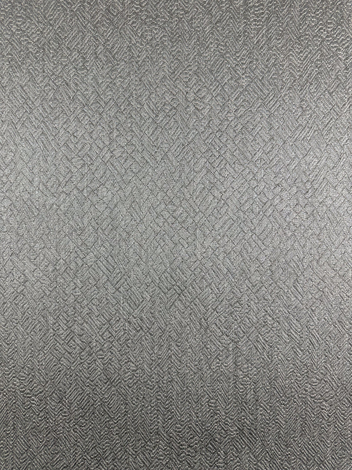 The Herringbone Textured Upholstery - Urbane Silver by Super Cheap Fabrics showcases a sophisticated, heavy-weight fabric with a metallic, reflective surface. Its intricate herringbone pattern, featuring intersecting lines, enhances its textured look and muted silver-gray hue. Width: 143cm.