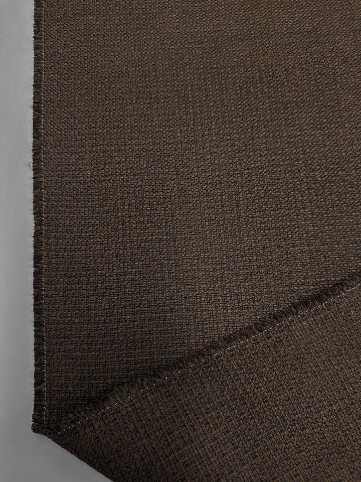 Close-up of Super Cheap Fabrics' Basket Weave Upholstery - Tuco - 147cm, a dark brown textured fabric with visible seam and frayed edge. Spread flat, this heavy-weight upholstery displays its intricate weave pattern in a neutral tone.