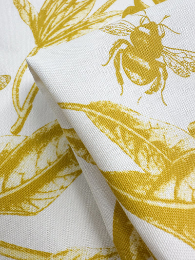 Close-up of Super Cheap Fabrics' Cotton Duck - Bee Mustard (150cm) showing its intricate print of bees and leaves on spicy mustard hue cotton fabric. The folded material highlights texture, ideal for adding a touch of nature to home décor.