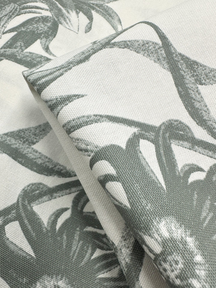 A close-up of the textured Cotton Duck - Bee Seagrass fabric by Super Cheap Fabrics reveals a medium-weight monochrome botanical pattern, featuring detailed gray leaves and flowers, perfect for an elegant home décor look against a light background.