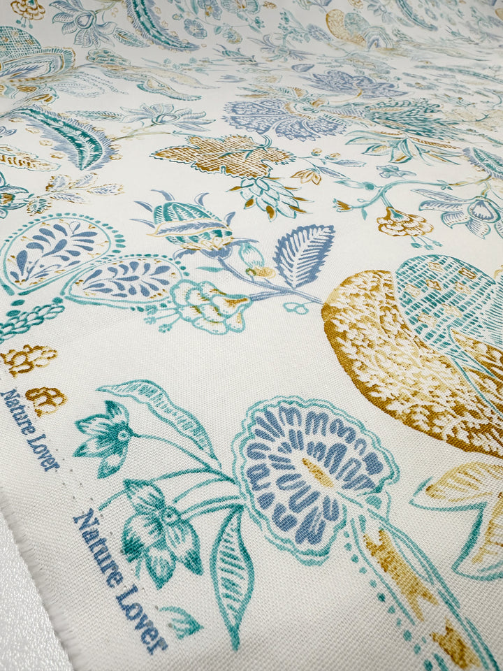 The Super Cheap Fabrics' Cotton Duck - Fine Lines (147cm) is a medium-weight cotton with turquoise, mustard, and blue floral designs on white. Ideal for home décor, it features "Nature Lover" artfully printed along the edge.