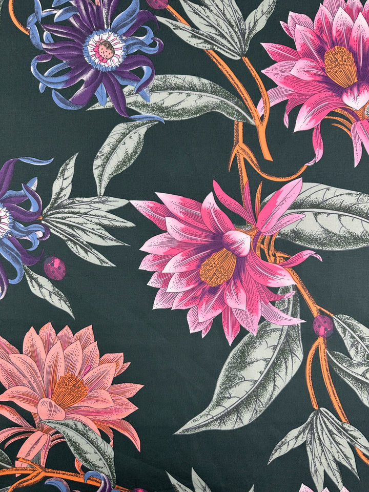 The Cotton Duck - Tropical Punch - 147cm by Super Cheap Fabrics showcases a vibrant floral pattern with pink, purple, and orange flowers on medium-weight cotton. Perfect for home décor, the fabric's intricate petals and lush green leaves stand out against its dark backdrop.