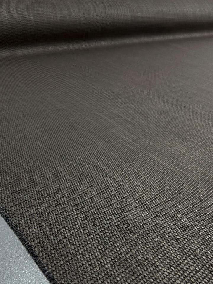 Close-up of Super Cheap Fabrics' Grid Upholstery - Yari 117 - 147cm, a dark, textured fabric roll with a subtle grid pattern. The smooth and evenly woven, high-durability material suggests it is ideal for heavy-weight upholstery; the out-of-focus background highlights its intricate details.