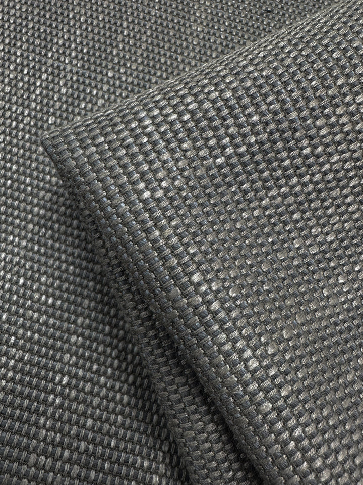 The Yari 117 - 147cm from Super Cheap Fabrics is a dark gray, heavyweight upholstery fabric with a textured, grid-like pattern reminiscent of lava smoke. It has a thick, sturdy appearance and a subtle sheen that highlights its high durability and quality.