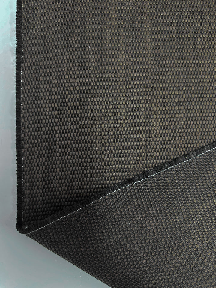 Close-up of Super Cheap Fabrics' Grid Upholstery - Yari 016 (147cm) featuring a high durability black and dark gray checkered pattern. The slightly folded corner highlights its thickness and weave, ideal for heavy-use furniture, set against a smooth white background.