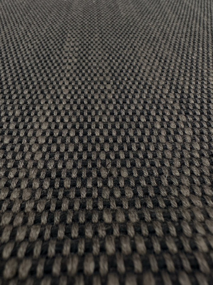 The Grid Upholstery - Yari 016 by Super Cheap Fabrics features a black and gray checkerboard texture with a tightly woven pattern for durability. Its repetitive dark and light squares create depth and movement, making it ideal for heavy-use furniture.