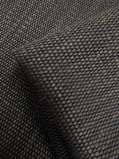 Close-up of Super Cheap Fabrics' Grid Upholstery - Yari 016 showcasing its textured black waffle weave. The fabric, layered with folds and shadows, highlights an intricate design suitable for heavy-use furniture due to its durability. Width: 147cm.