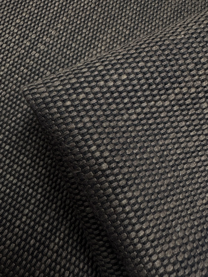 Close-up of Super Cheap Fabrics' Grid Upholstery - Yari 016 showcasing its textured black waffle weave. The fabric, layered with folds and shadows, highlights an intricate design suitable for heavy-use furniture due to its durability. Width: 147cm.