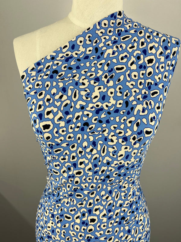 A mannequin showcases a form-fitting, one-shoulder dress using Super Cheap Fabrics' Printed Lycra - Blue Reef. This medium-weight fabric features blue, white, and black leopard spots on a neutral gray background.