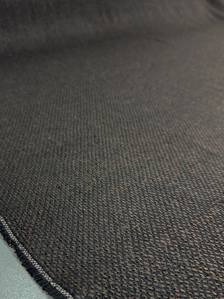 The Designer Tweed - Choco by Super Cheap Fabrics features a textured, dark woven polyester with a nearly black and brown mix. This heavy-weight fabric's detailed weave and slightly frayed edge make it ideal for crafting durable outer coats.
