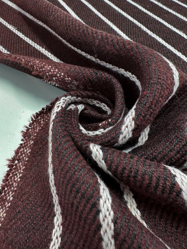 Close-up of Super Cheap Fabrics’ Designer Tweed - Plum Line, 155cm wide, showcasing heavy weight fabric with maroon, gray, and white stripes in a spiral pattern. Its soft and fuzzy texture highlights the weave's detailed contrast—ideal for cozy outer coats.
