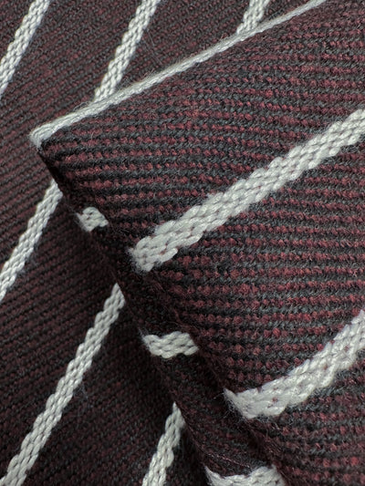 Close-up of Designer Tweed - Plum Line - 155cm by Super Cheap Fabrics, showcasing a textured, heavy weight fabric with a dark red and black weave and diagonal white stripes. The folded polyester material highlights its rugged, tactile appearance from various angles.