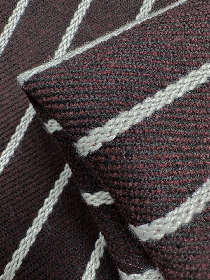 Close-up of Designer Tweed - Plum Line - 155cm by Super Cheap Fabrics, showcasing a textured, heavy weight fabric with a dark red and black weave and diagonal white stripes. The folded polyester material highlights its rugged, tactile appearance from various angles.
