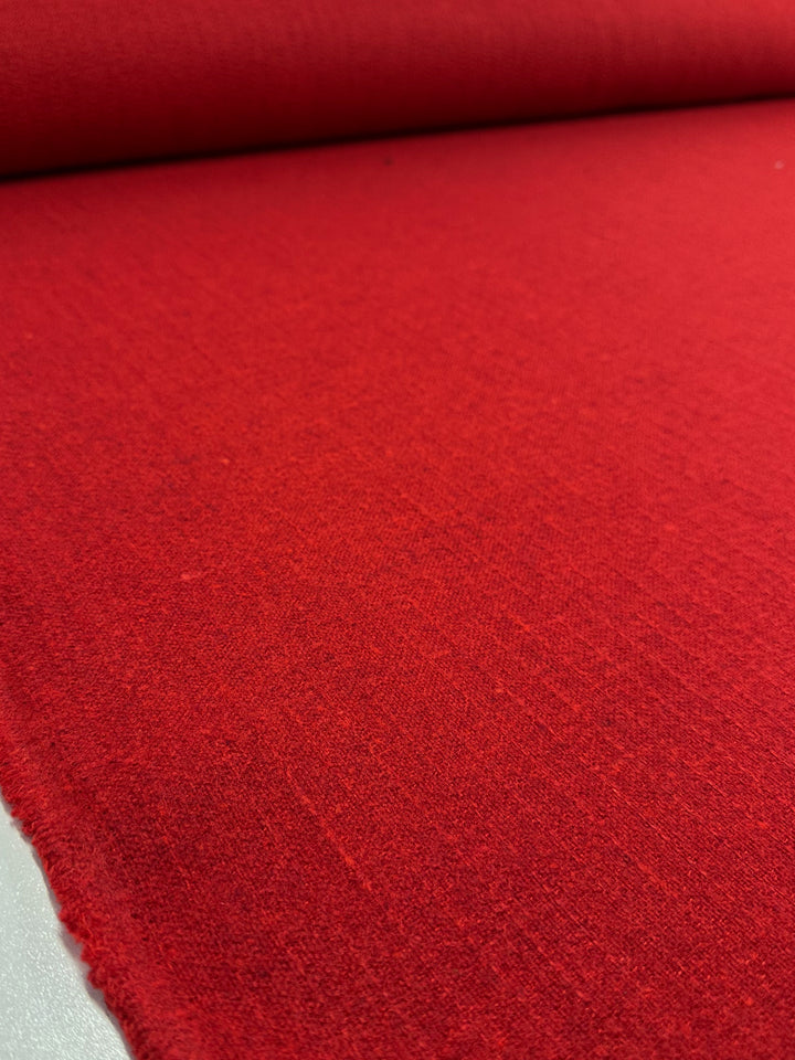 A close-up of Super Cheap Fabrics' Brushed Tweed - Flame - 150cm shows vibrant scarlet fabric, smooth and unrolled. The slightly frayed edge reveals its high-quality polyester nature, ideal for various textile applications.