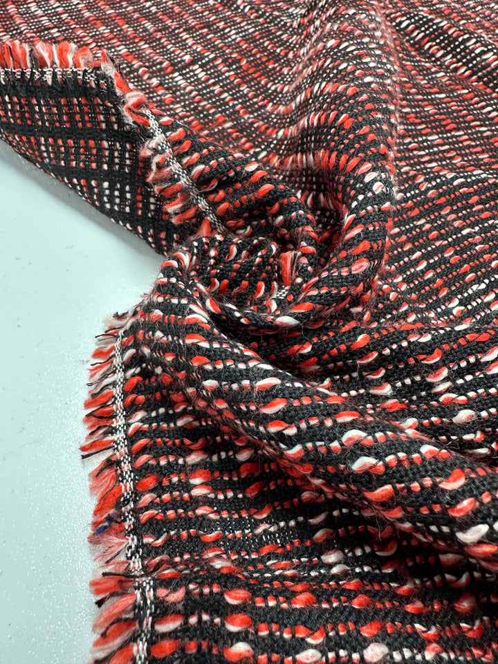 The Designer Tweed - Ripple Red - 157cm by Super Cheap Fabrics features interlaced black, red, and white threads. This medium-weight fabric has a textured weave with fringed edges on a smooth, light-colored surface, ideal for outer coats or jackets.