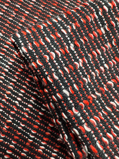 Close-up of Designer Tweed - Ripple Red by Super Cheap Fabrics, featuring a woven pattern in black, white, and red threads. With a textured grid-like design ideal for coats and jackets, this medium weight fabric creates a dynamic look. Part of the 157cm fabric is folded over itself.