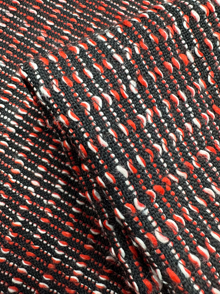 Close-up of Designer Tweed - Ripple Red by Super Cheap Fabrics, featuring a woven pattern in black, white, and red threads. With a textured grid-like design ideal for coats and jackets, this medium weight fabric creates a dynamic look. Part of the 157cm fabric is folded over itself.