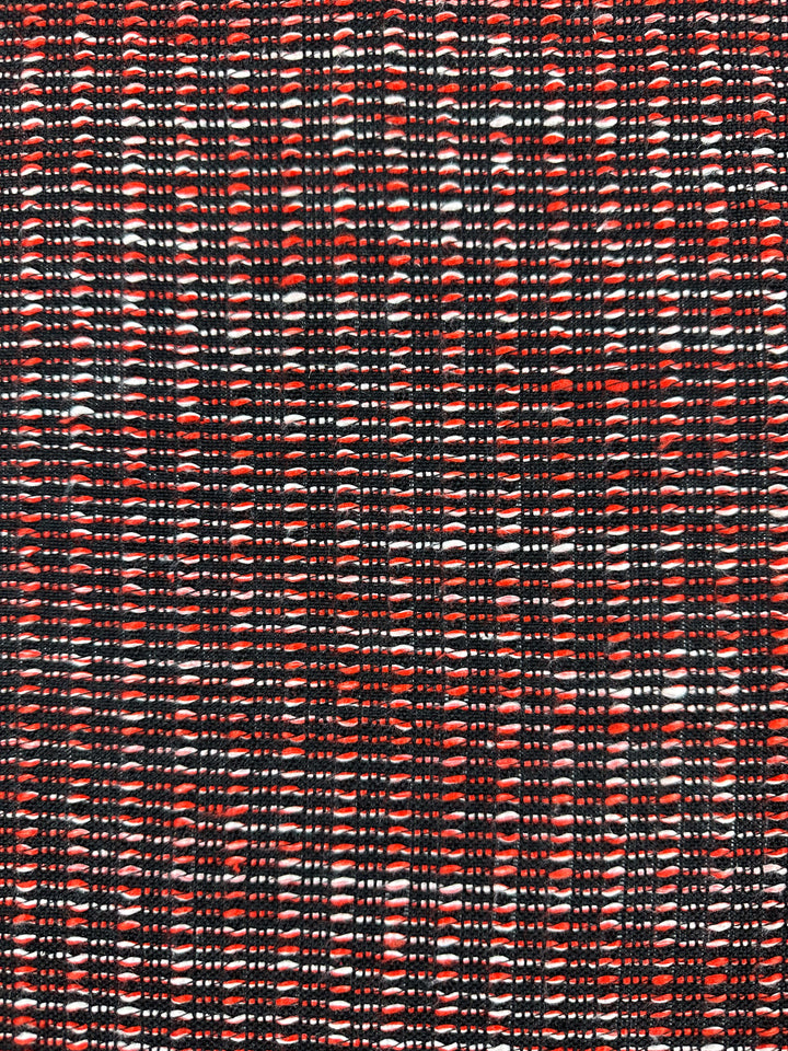Close-up of Designer Tweed - Ripple Red - 157cm by Super Cheap Fabrics. This fabric, perfect for jackets, features a red and black woven pattern with white accents, creating a textured design ideal for medium weight applications.