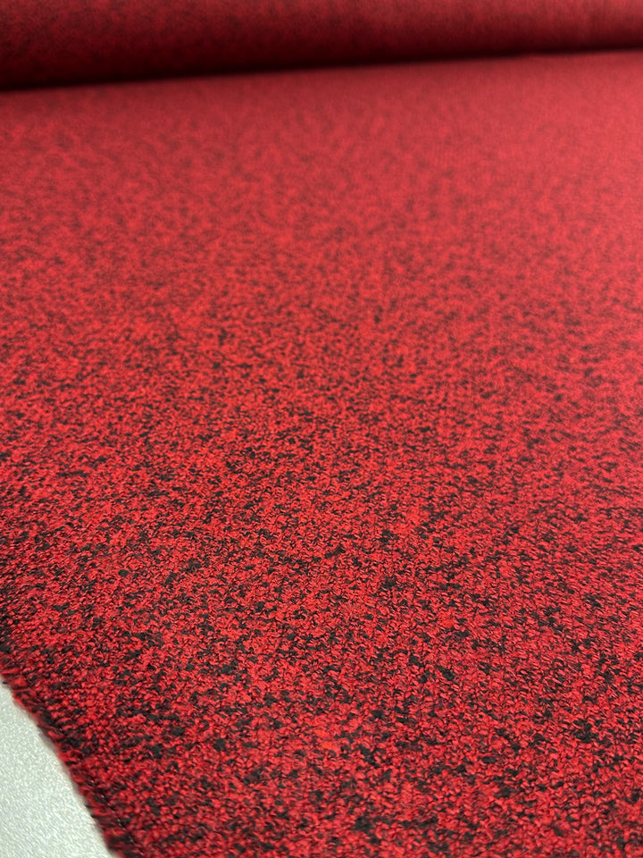 Close-up of Super Cheap Fabrics' Designer Tweed - Serpents (150cm), featuring a red heavyweight textured black pattern resembling speckled tweed. Ideal for outer coats, this polyester material is shown unrolled on a flat surface.