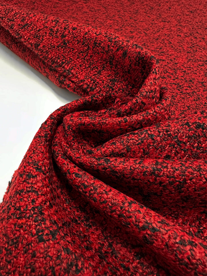 A close-up of Designer Tweed - Serpents by Super Cheap Fabrics shows a textured red and black heavyweight weave. Gently folded, the 150cm wide polyester fabric highlights its rich texture and color variation, perfect for outer coats.