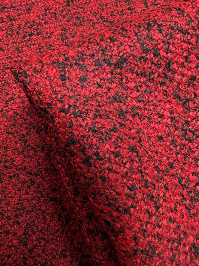 The Designer Tweed - Serpents by Super Cheap Fabrics features a close-up of red and black textured fabric with a looped woven pattern. Perfect for outer coats, this heavyweight polyester is thick, soft, and radiates warmth and comfort with its intricate design and vibrant colors. Width: 150cm.