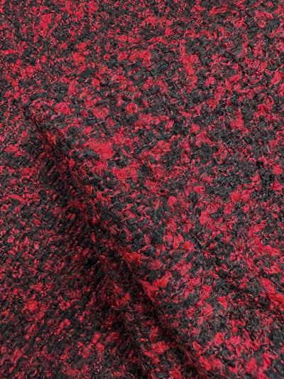Close-up of Super Cheap Fabrics' Designer Tweed in Red Fluff. This 150cm polyester blend fabric features a red and black boucle pattern with loops for a soft, slightly rough surface, ideal for heavy-weight outer coats with rich speckled colors.