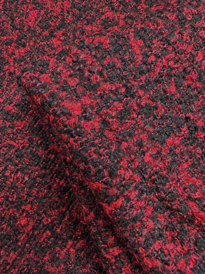Close-up of Super Cheap Fabrics' Designer Tweed in Red Fluff. This 150cm polyester blend fabric features a red and black boucle pattern with loops for a soft, slightly rough surface, ideal for heavy-weight outer coats with rich speckled colors.