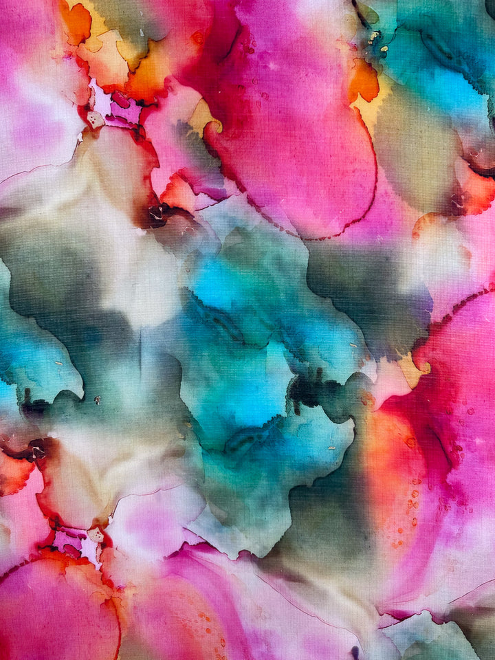 The Designer Cotton - Monique from Super Cheap Fabrics features a vibrant abstract pattern with splashes of pink, blue, orange, and green. These blend in fluid shapes reminiscent of luxury sewing projects, creating dynamic movement and depth across its 150cm width.