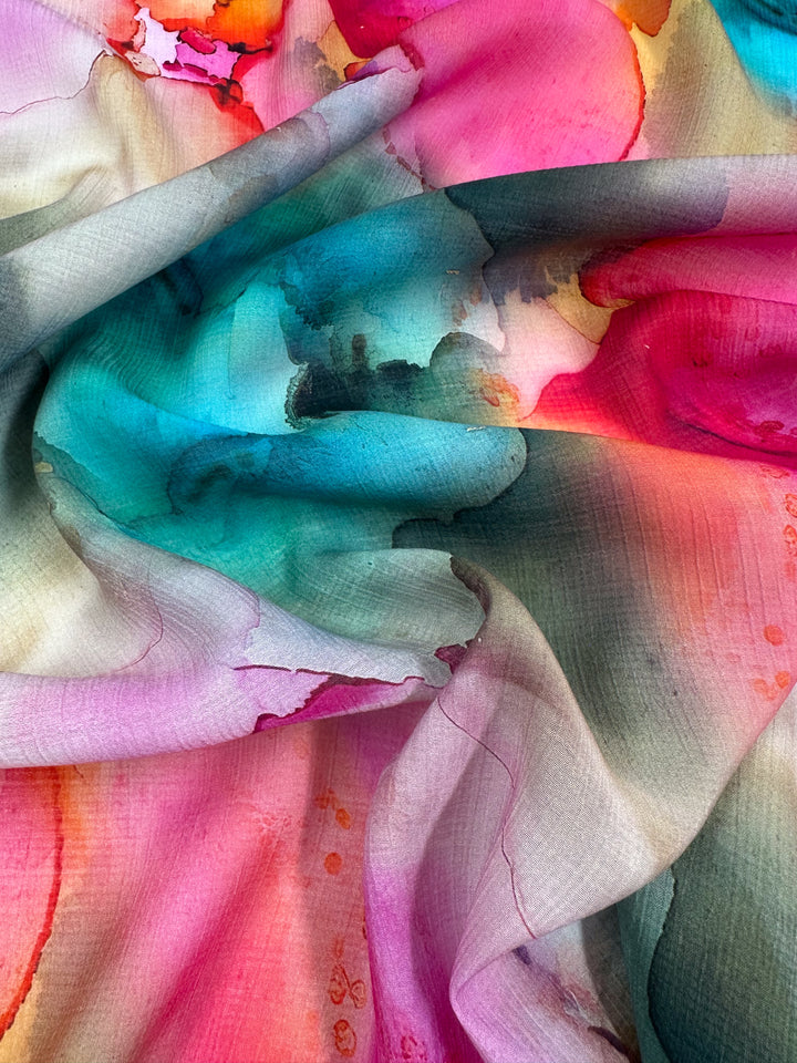 A close-up of the Designer Cotton - Monique - 150cm from Super Cheap Fabrics reveals a watercolor-like pattern featuring vibrant hues of blue, pink, red, orange, and green. The colors blend seamlessly to create a fluid and artistic appearance ideal for luxury sewing projects.
