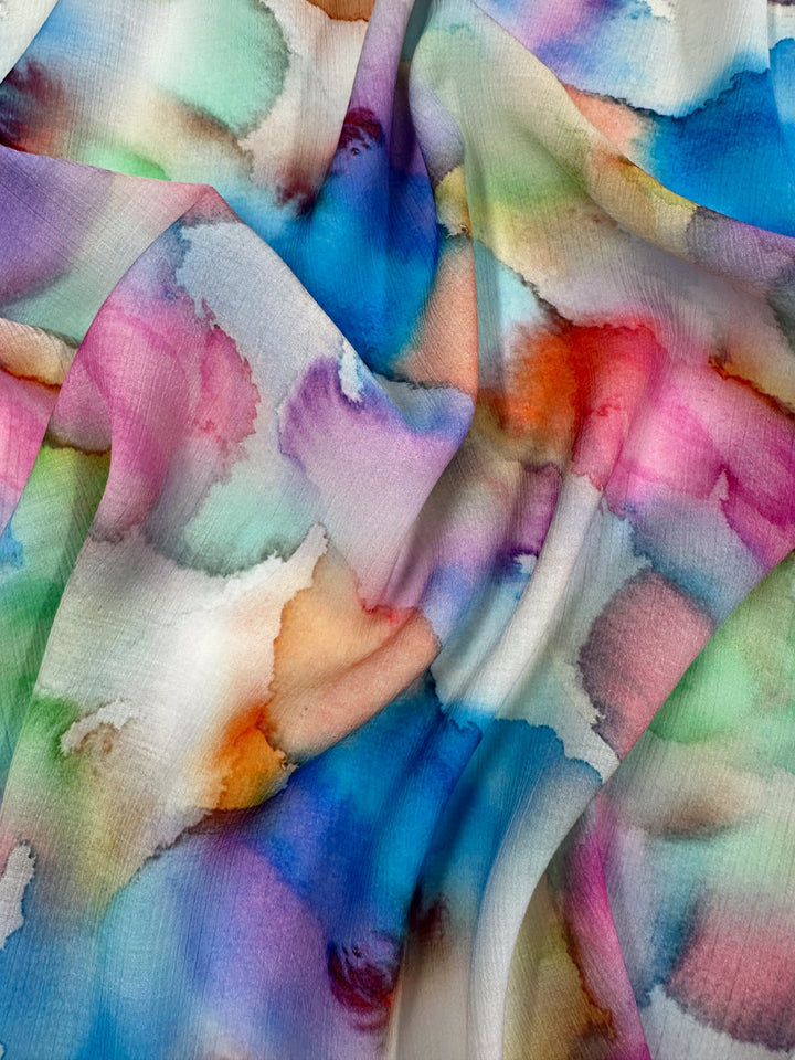 The Designer Cotton - Airbrush - 150cm by Super Cheap Fabrics is a luxury fabric featuring a colorful watercolor pattern with blended swirls of blue, pink, green, orange, and purple, ideal for sewing projects needing a vibrant and artistic touch.