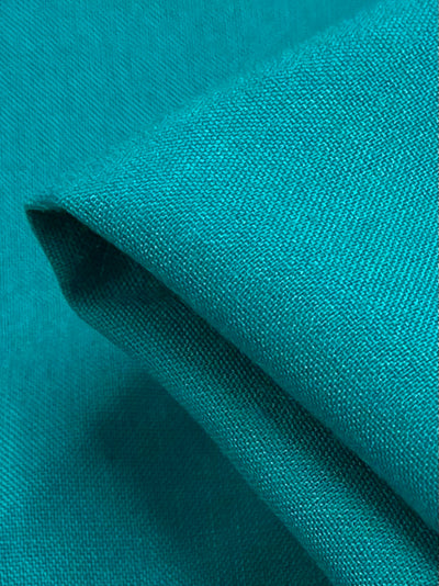 A close-up of Plain Rayon - Columbia - 145cm by Super Cheap Fabrics in teal blue, showing its lightweight, smooth surface and visible weave texture with a neatly folded edge.