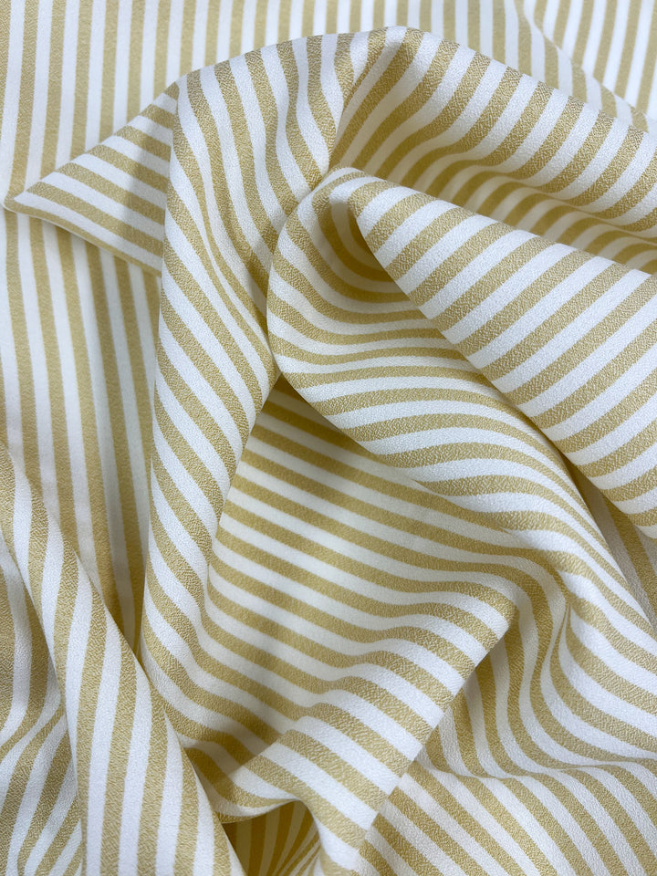 A close-up of Striped Crepe - Raffia (150cm) from Super Cheap Fabrics, featuring lightweight polyester with beige and white diagonal stripes, soft folds, and a smooth texture.
